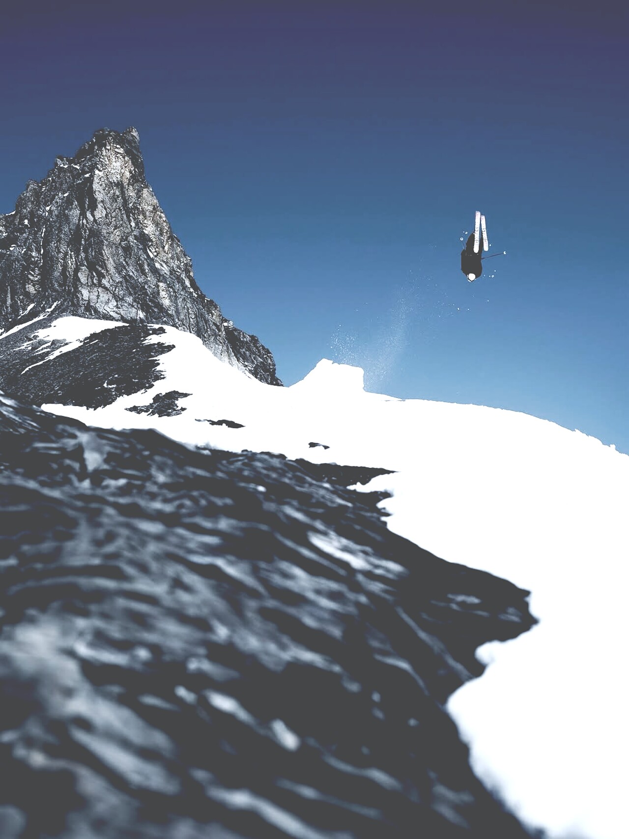 A skier mid-air above a granite spire under deep blue sky